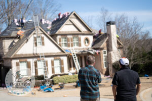 A project manager and homeowner watch as a new roof is being installed